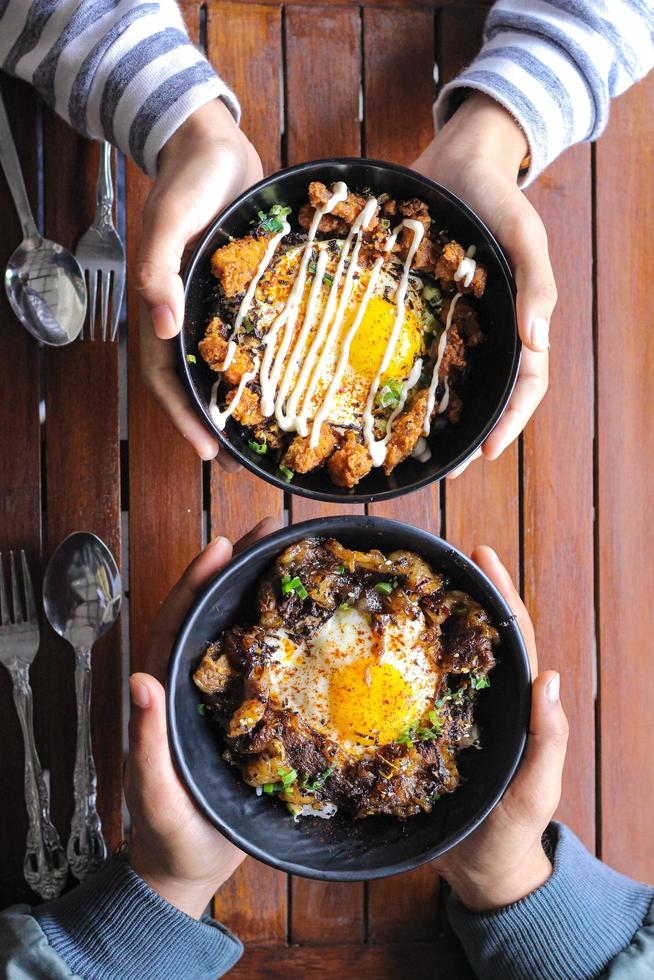Rice with fried egg and chicken fries in black bowl on wooden table photo