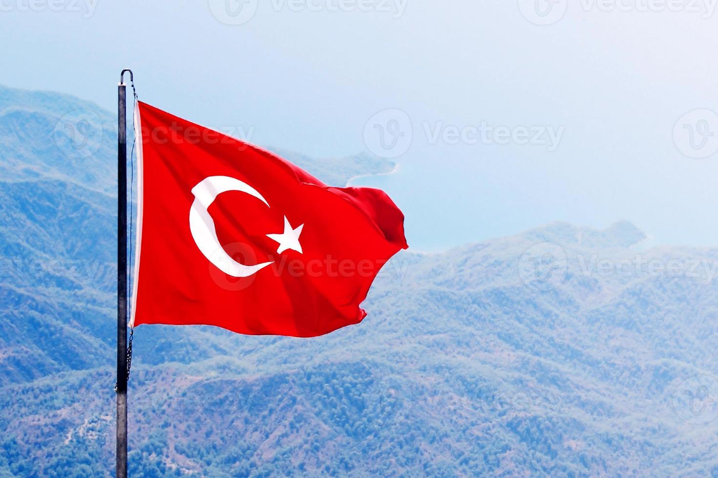 Red Turkey flag against mountains and sea, closeup photo