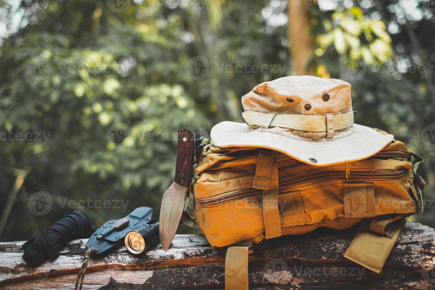 Equipment for survival bucket hat backpack hiking knife camping flashlight resting on wooden timber in the background is a forest photo