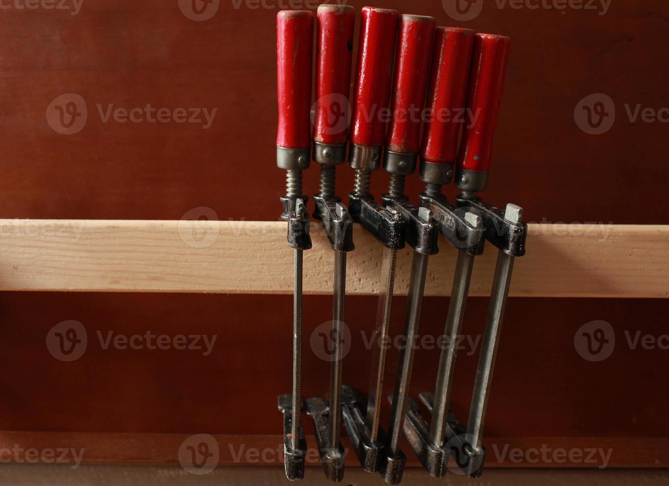 row of clamps with red handles hang on a shelf in a carpentry workshop photo