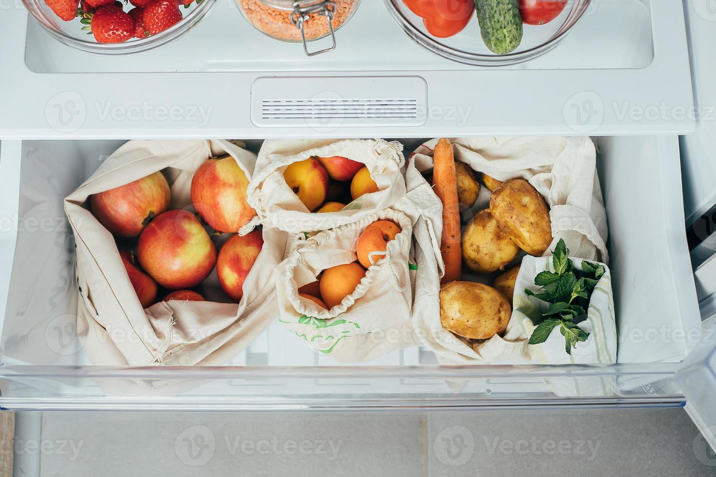 Zero waste concept. Fresh vegetables and fruits in eco cotton bags in a refrigerator from market. photo