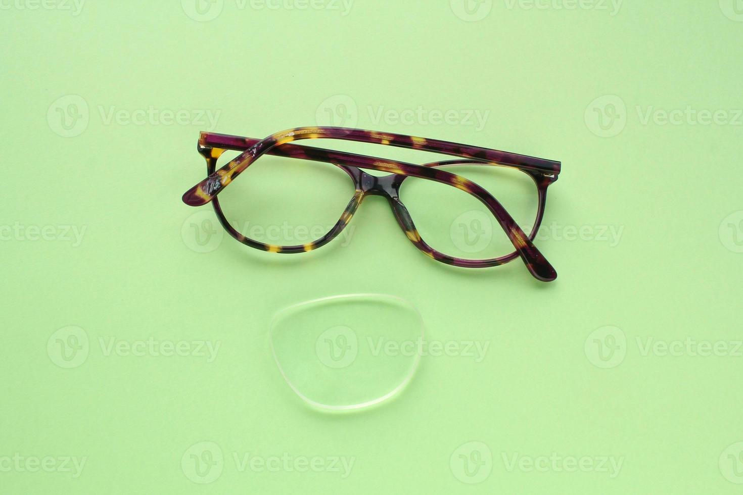 Old broken eyeglasses with damaged lens on green background. Poor eyesight. Reuse and repair concept. Idea of health. Failure optic eyewear. Breakage of vision correction glasses. Close up, flat lay photo