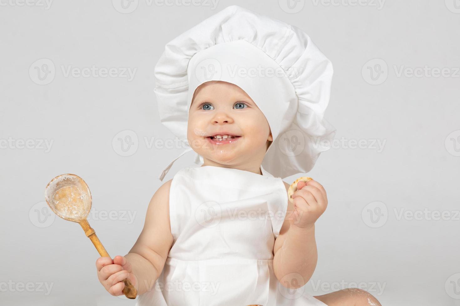 Child cook. Beautiful little girl in cook clothes with a big spoon. The child is one year old. Funny baby is laughing. Little chef. The concept of cooking food. photo