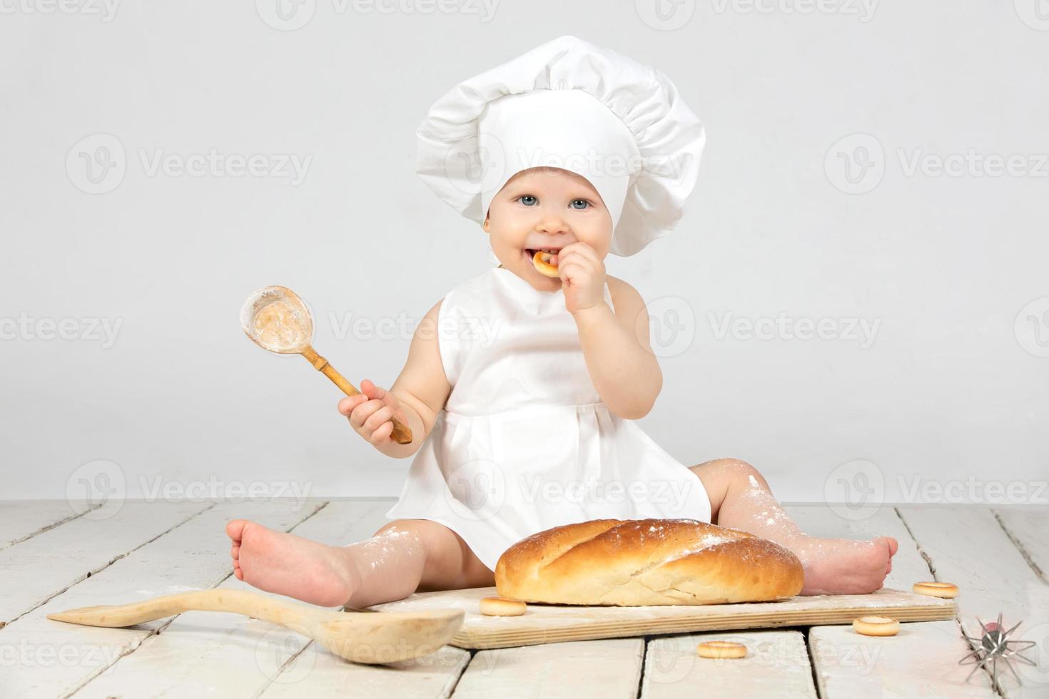 Child cook. Little girl in cook clothes with a big bun and flour. The girl is one year old. A child with an Easter bun. Funny kid in a culinary hat. photo