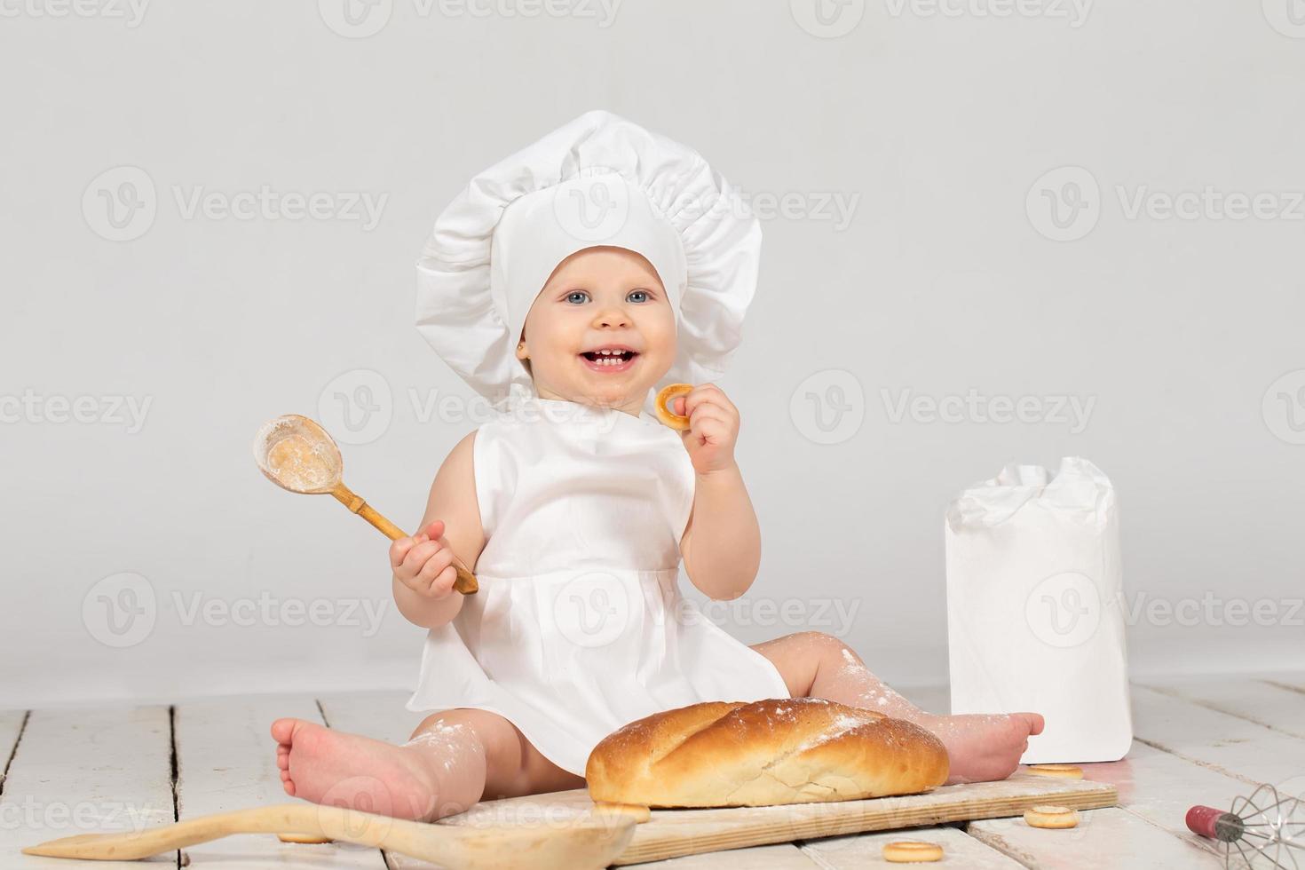 Baby cook. Beautiful little girl in cook clothes with a long loaf and a wooden spoon. The child is one year old. Funny baby. photo