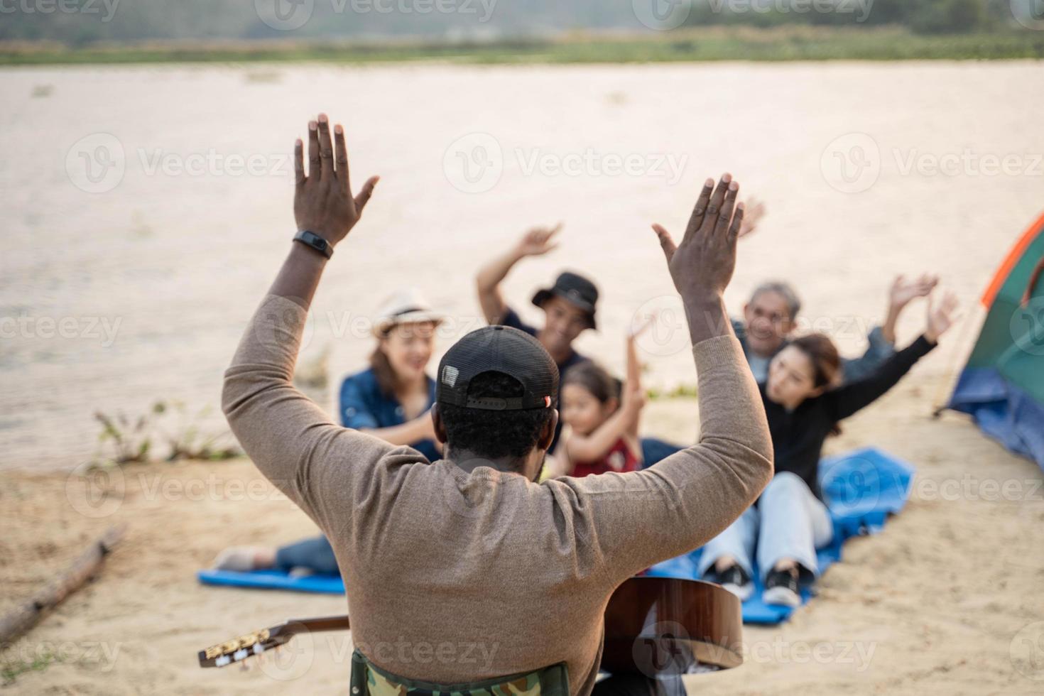 espalda ver a africano hombre tener divertido jugando guitarra con amigo cámping a el playa. canto , reír, jugando guitarra foto