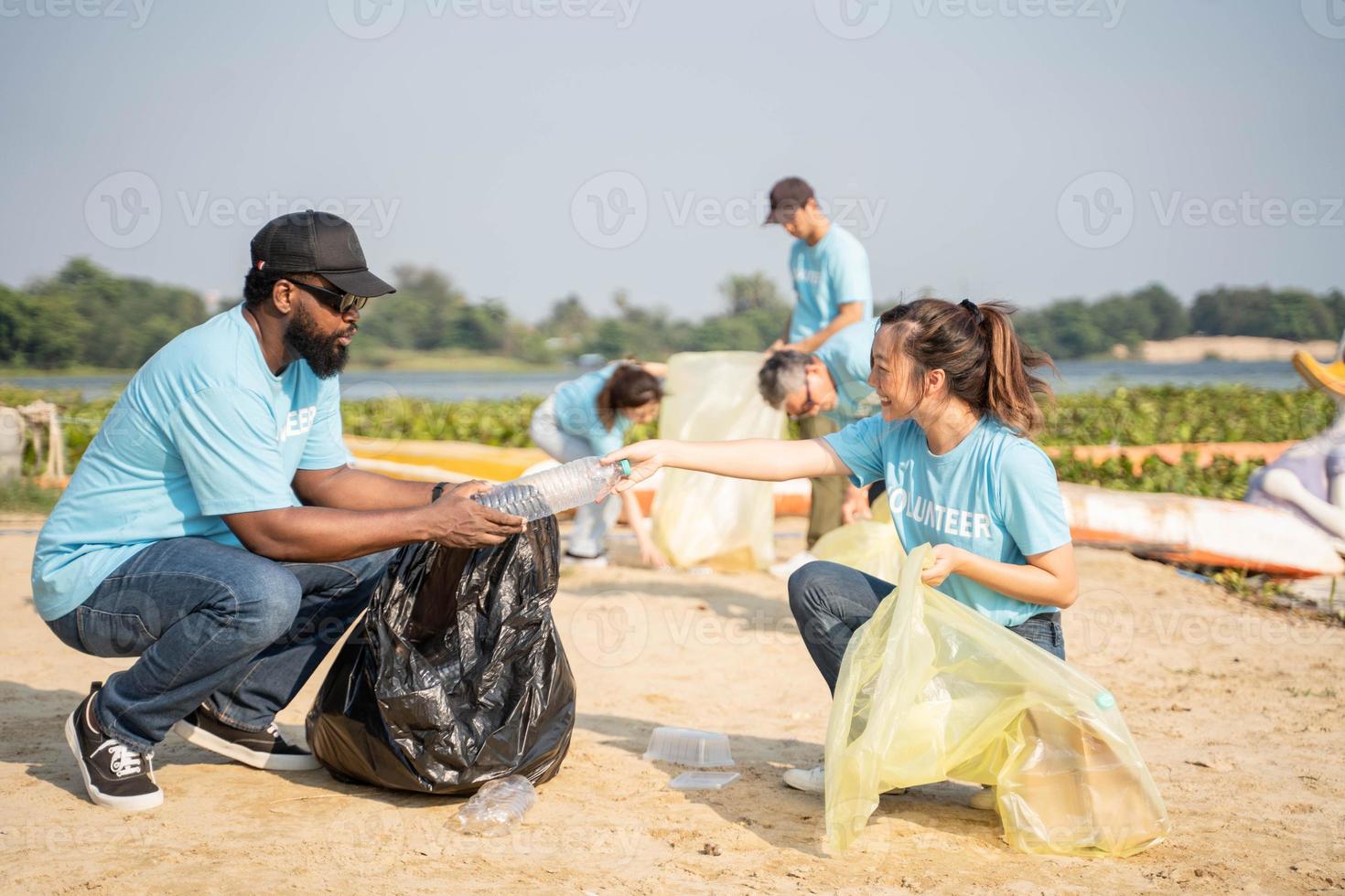 trabajar como voluntario, caridad, limpieza, personas y ecología concepto - grupo de contento voluntarios con basura pantalones limpieza zona en arenoso costa. foto