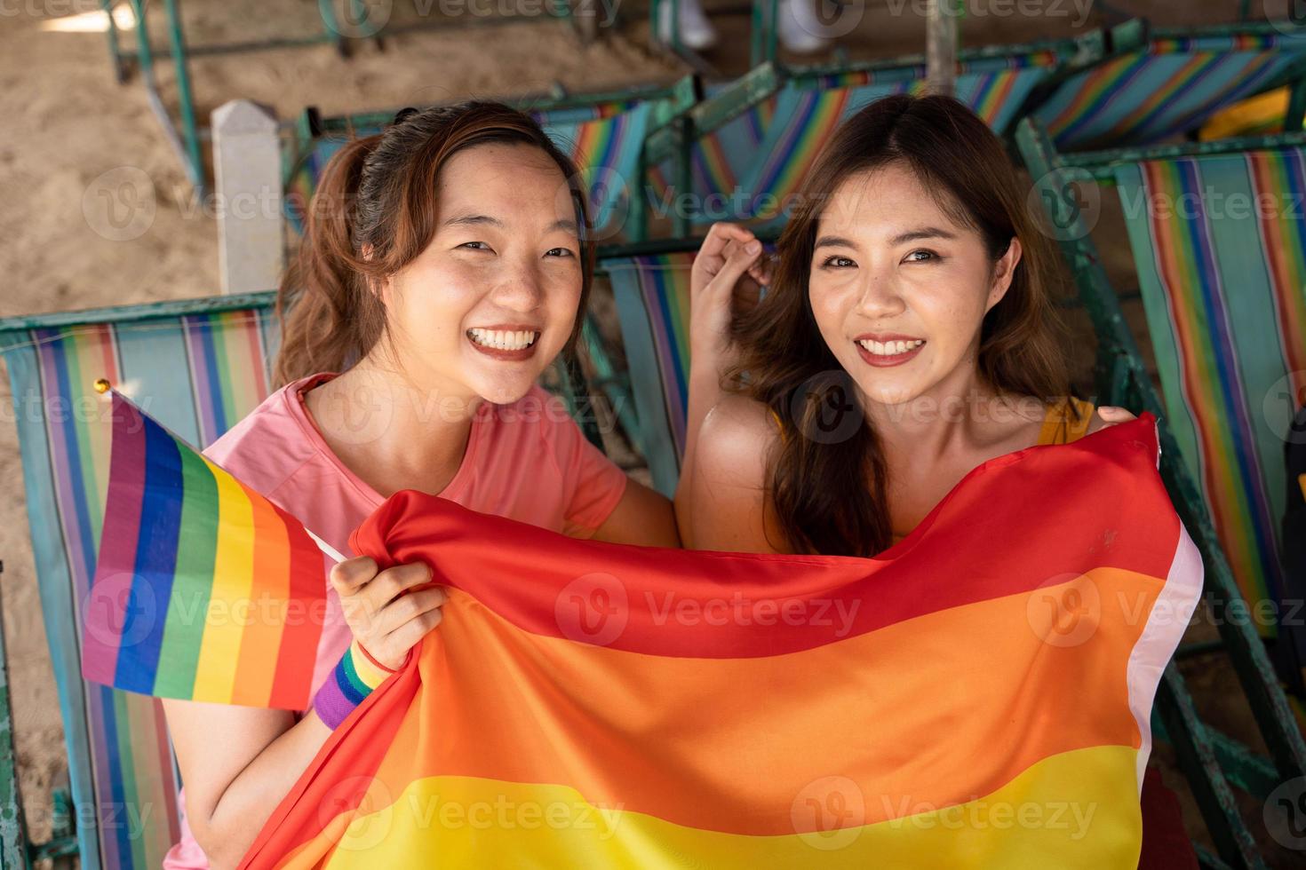 Happy lesbian, beautiful asian young two women, girl gay, couple love moment spending good time together, holding the LGBT flag on the beach. Supporters of the LGBT community photo