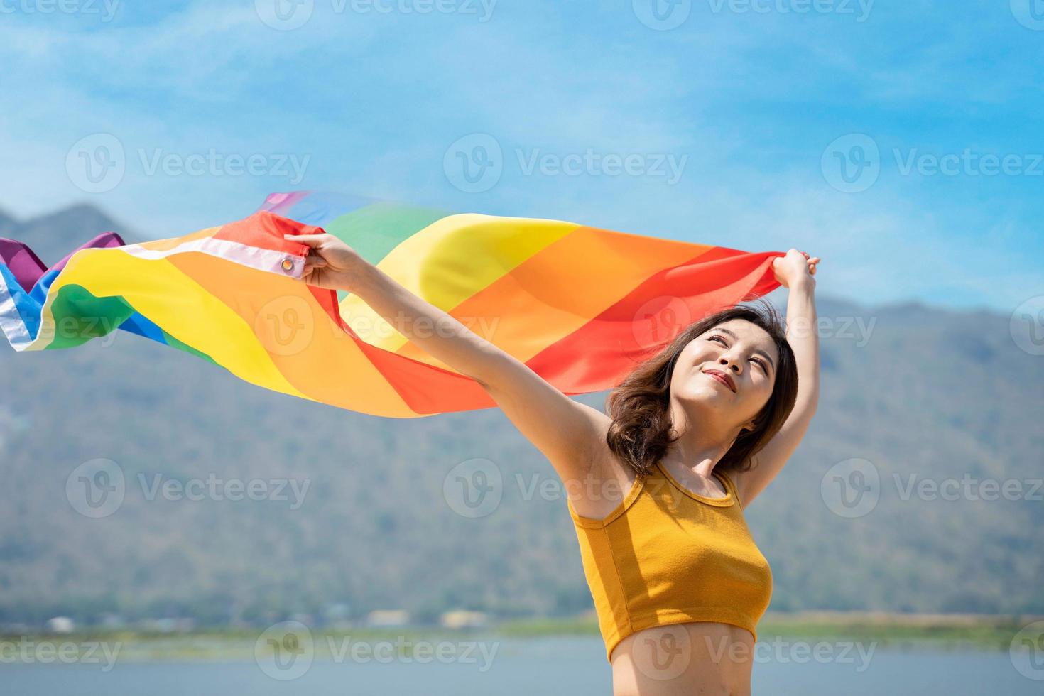 Lesbian women with gay pride rainbow flag on the beach against the sky. Young lesbian girls holding a rainbow flag and hugging happily. Supporters of the LGBT community photo
