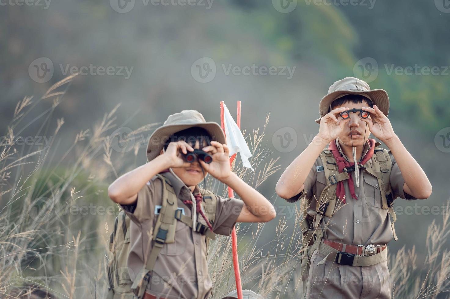 American Boy Scouts in uniform sit binoculars in a green field on a mountain hike going to summer camp. photo