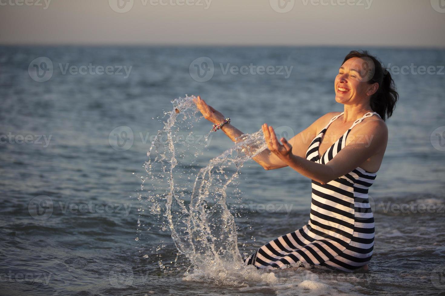 descanso a el complejo. mayor mujer en vacaciones por el mar con rociar de agua.curación mar agua. foto