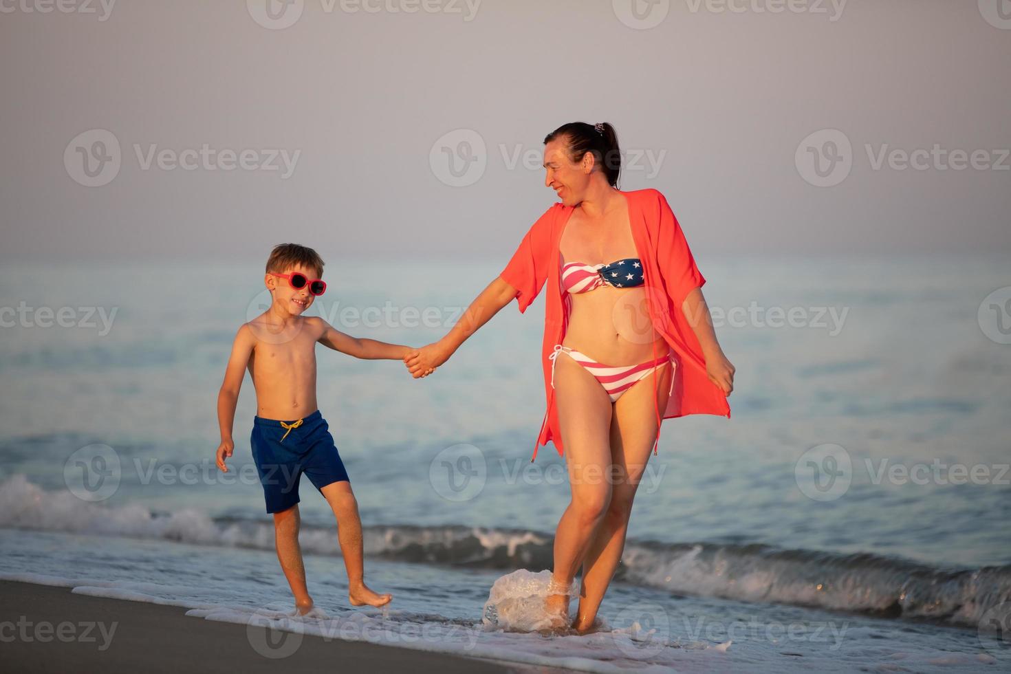 mamá y hijo a mar. un americano mujer con un pequeño chico caminar a lo largo el océano. foto