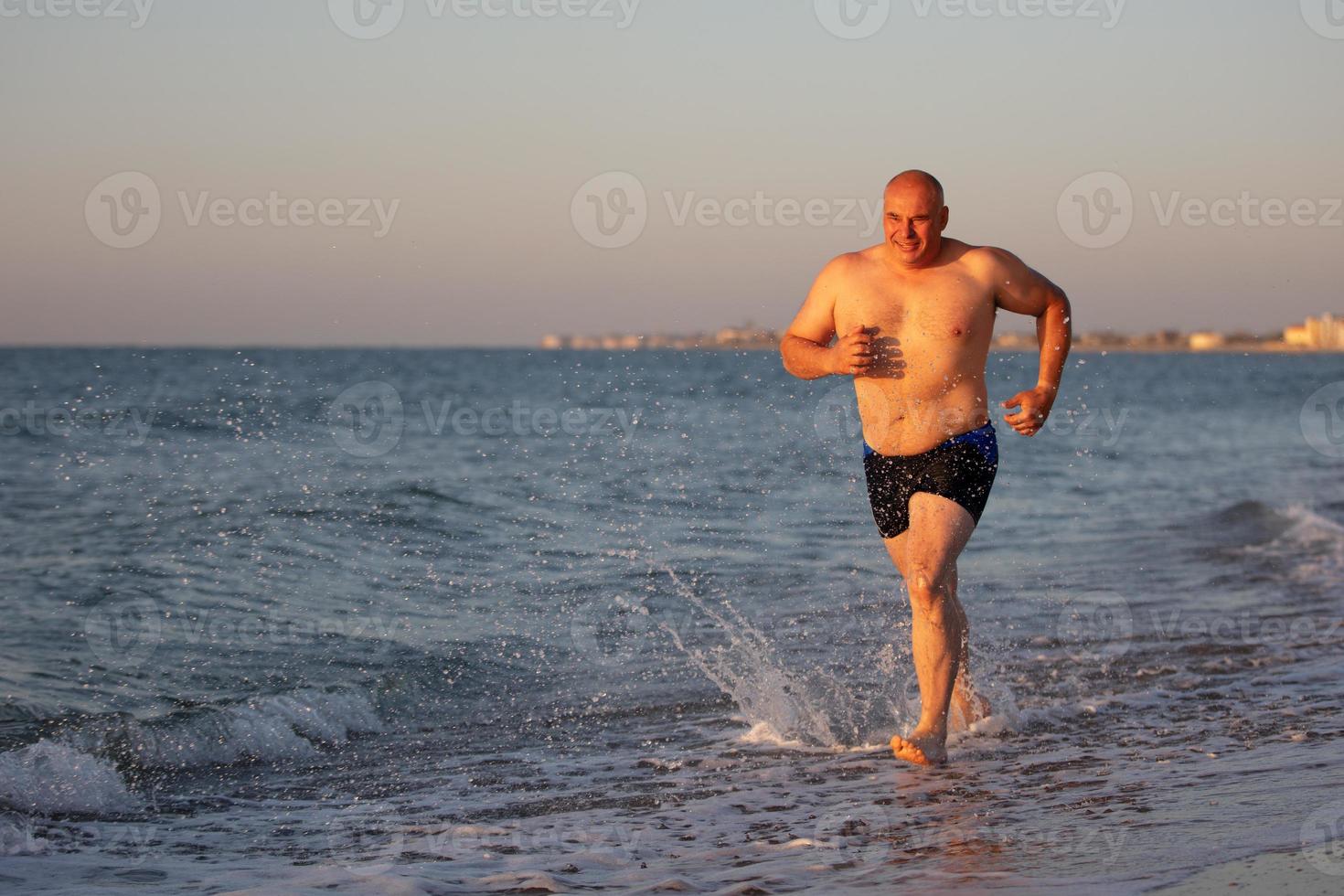 A middle-aged man jogs along the seashore. photo