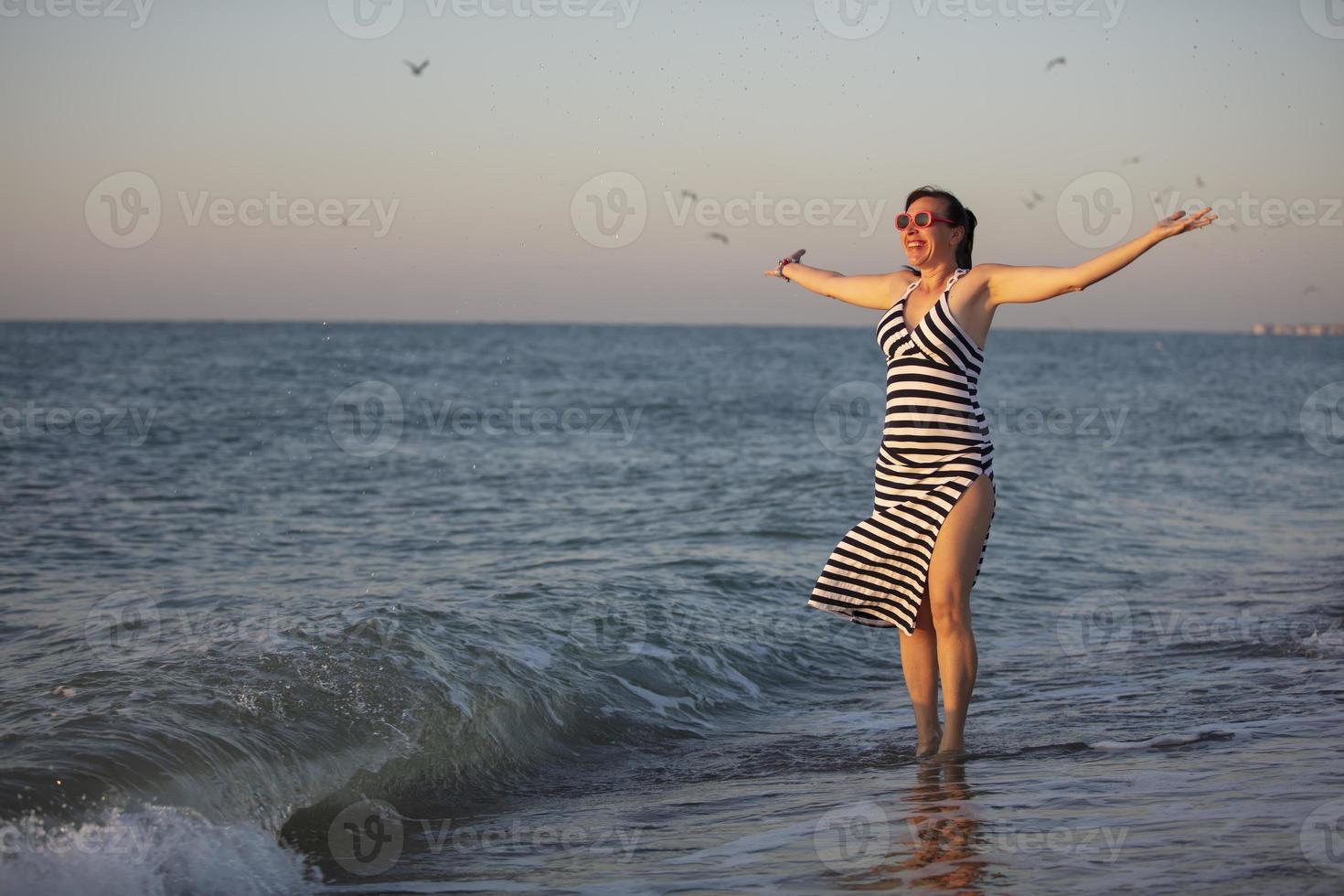 Happy middle aged woman by the sea with hands up. photo