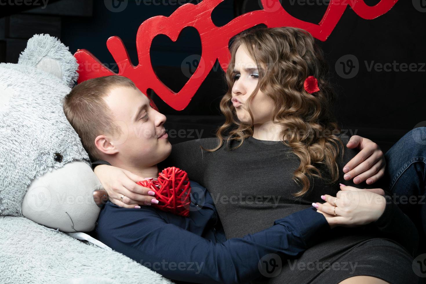 Loving girl and boyfriend on Valentine's Day. A young couple with a soft bear and a red rose lies on the floor. The girl and the guy are flirting. photo