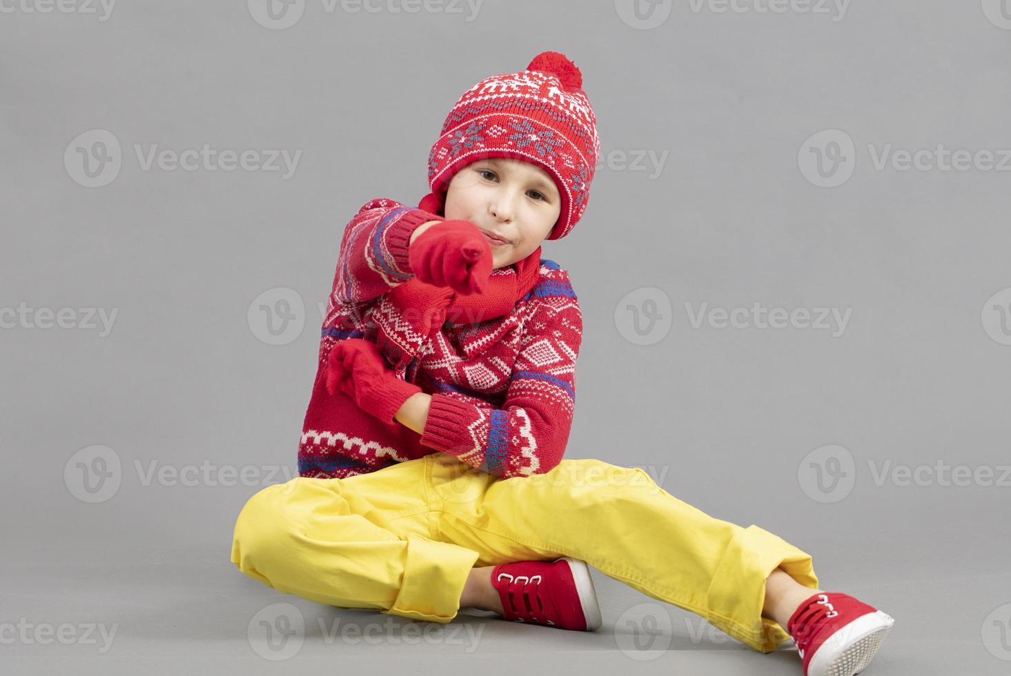 Child in warm knitted clothes on a studio background. A boy in a red hat and sweater. Fashionable boy in the studio. photo