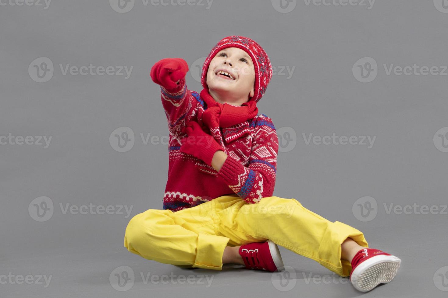 Child in warm knitted clothes on a studio background. A boy in a red hat and sweater. Fashionable boy in the studio. photo