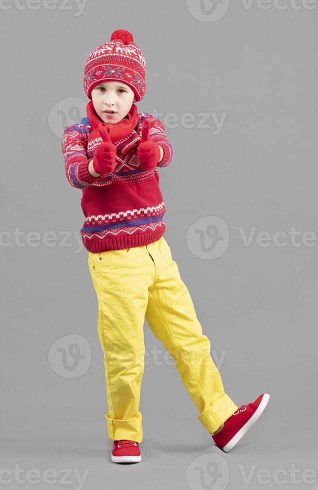 A child in warm, bright clothes. Boy in winter hat, scarf and red sweater and sneakers. Fashionable boy in the studio. photo