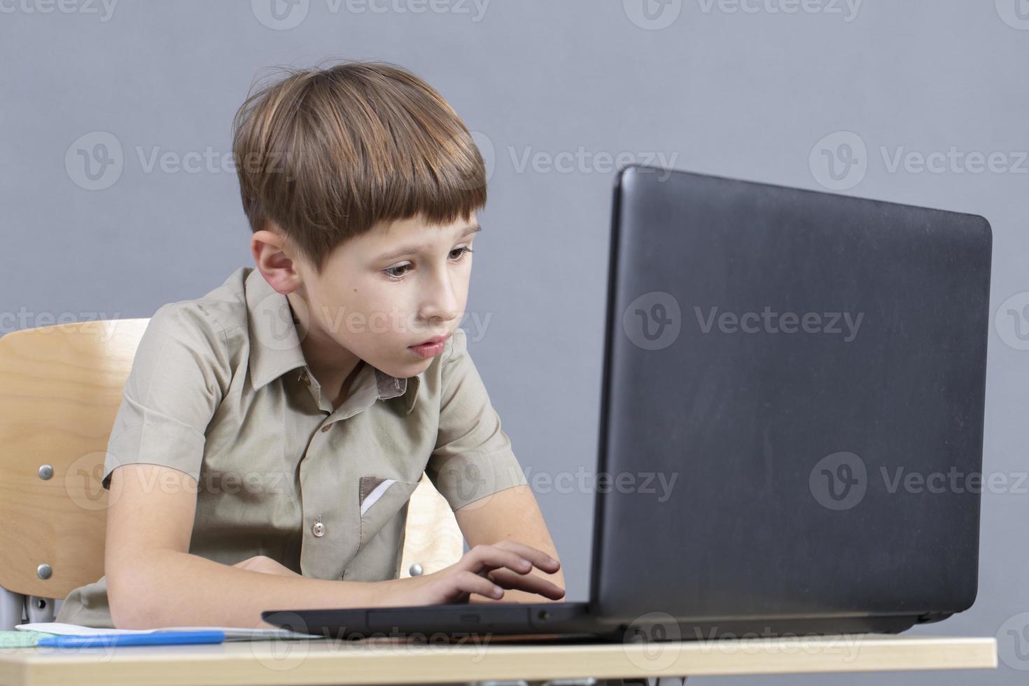 The child at the laptop. The boy looks at the monitor screen. Preschooler at the computer. Junior student at a table with a computer. photo