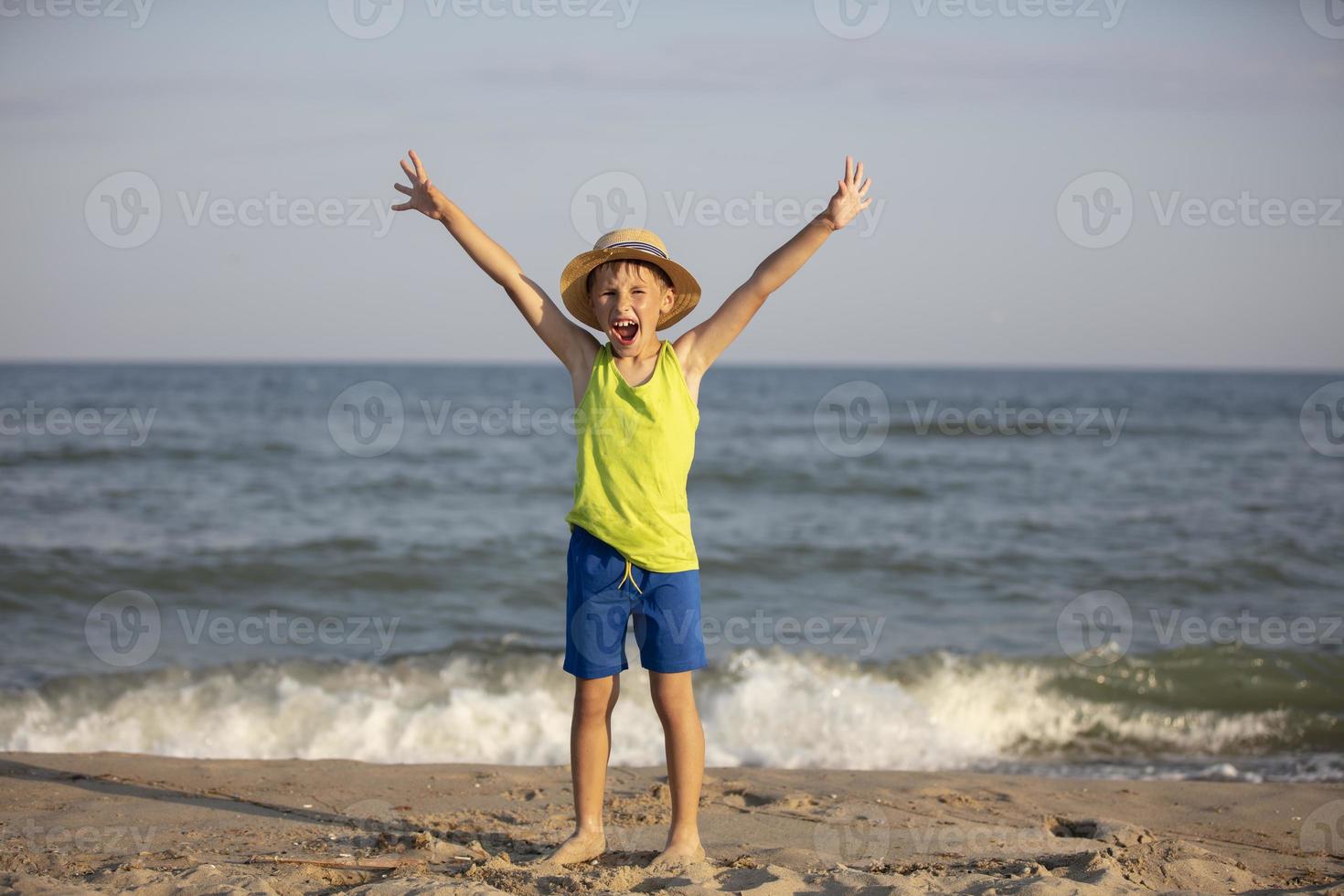 Happy child at sea. The boy on the coast raised his hands up. photo