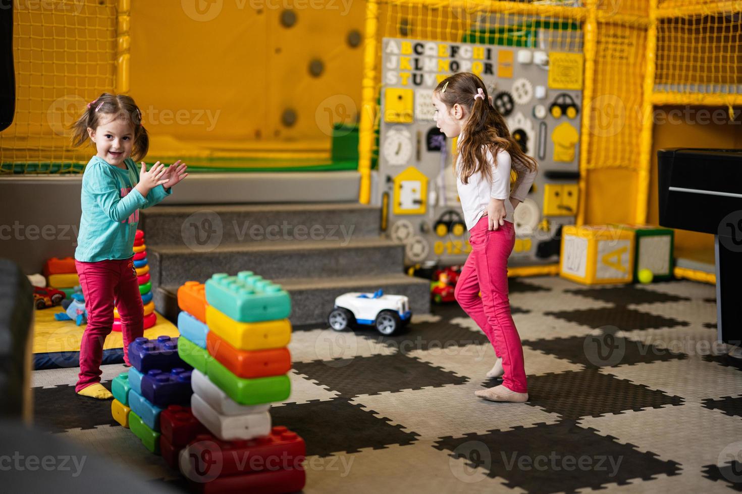 Two sisters playing at kids play center while build with colored plastic blocks. photo