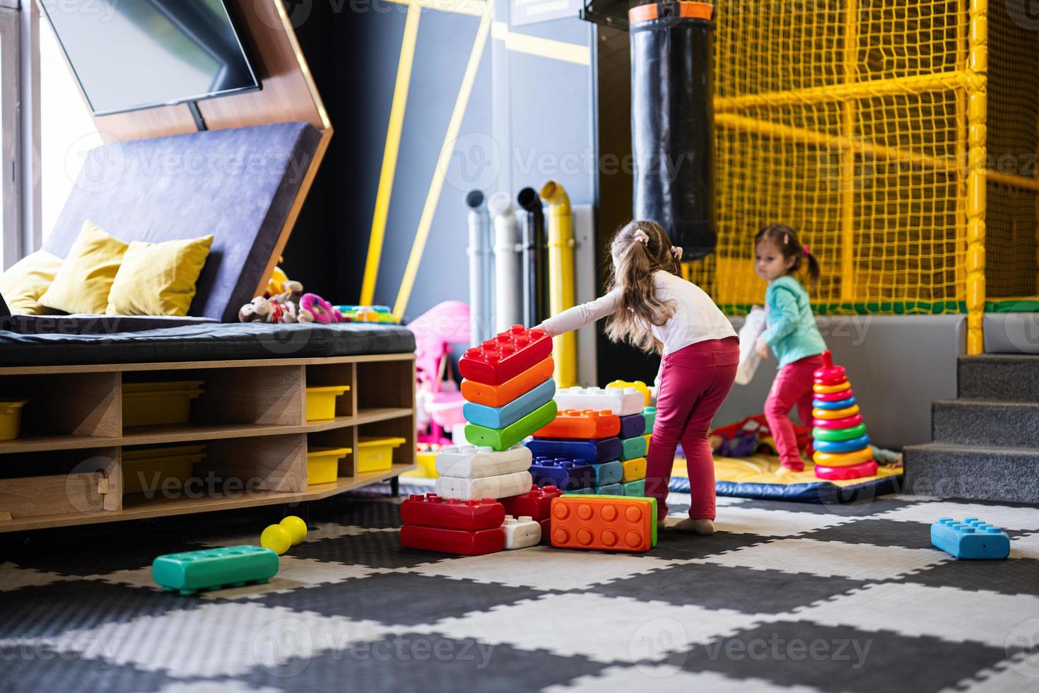 Two sisters playing at kids play center while build with colored plastic blocks. photo