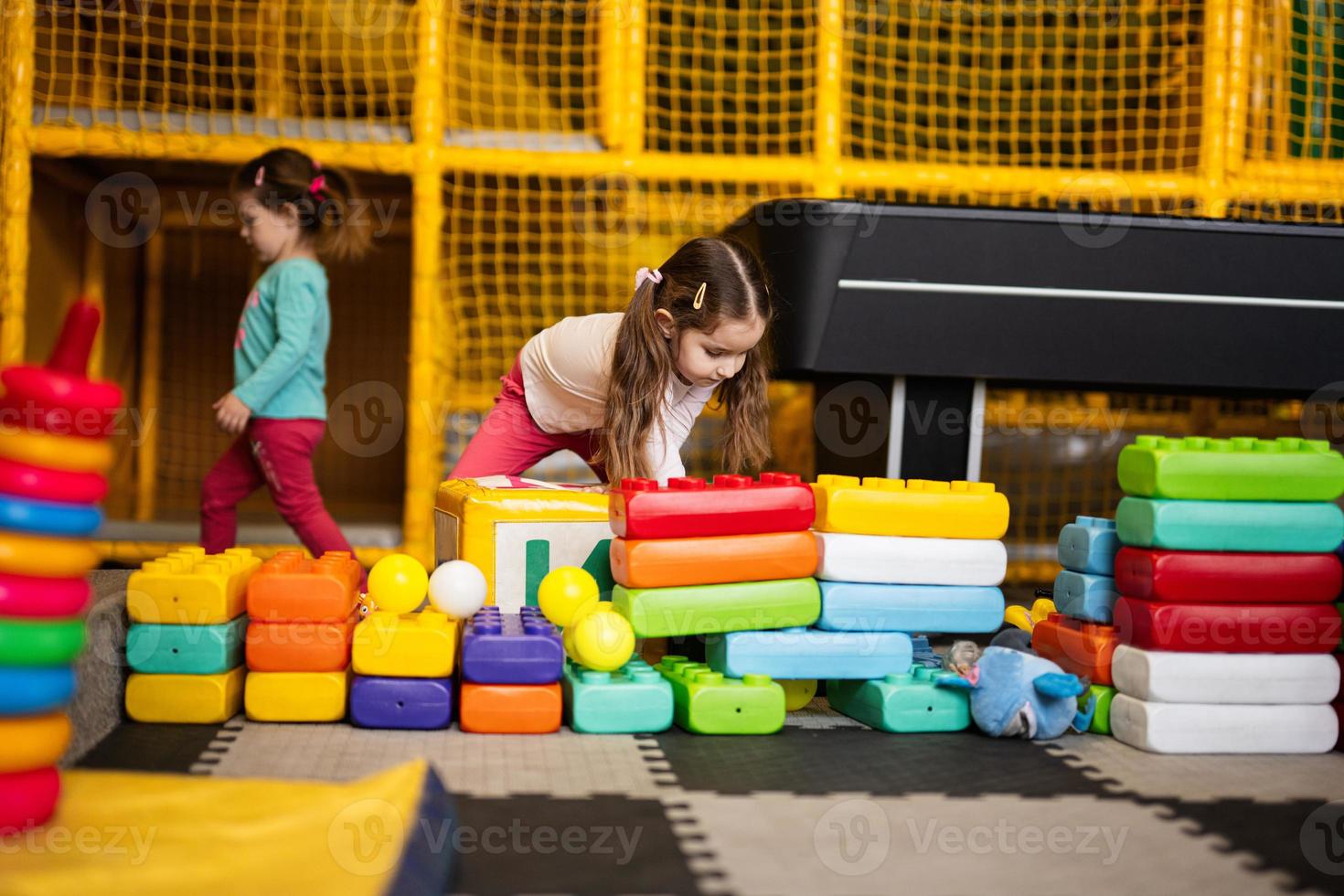 Two sisters playing at kids play center while build with colored plastic blocks. photo