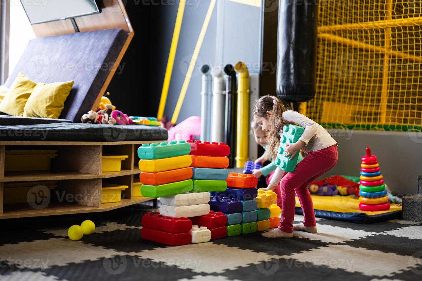 Two sisters playing at kids play center while build with colored plastic blocks. photo