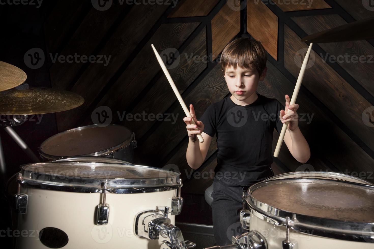 A boy is playing with a drumstick. The child behind the drum kit. photo