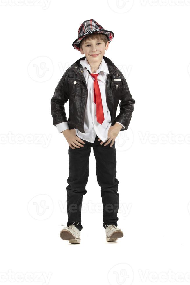 Fashionable boy in eight height on a white background. Child in a hat a leather jacket with a red tie. Funny elementary school student. photo