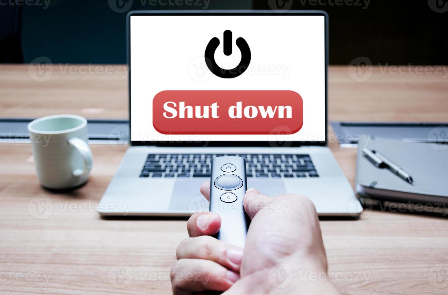 Businessman hand hold remote control with red button message Shut down and black icon on display laptop photo