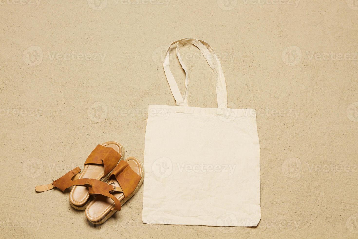 Mockup shopper handbag beach sand background. Top view copy space shopping eco reusable bag. Sandals accessories. Template blank top view white cotton material canvas cloth. Empty mock-up beach photo