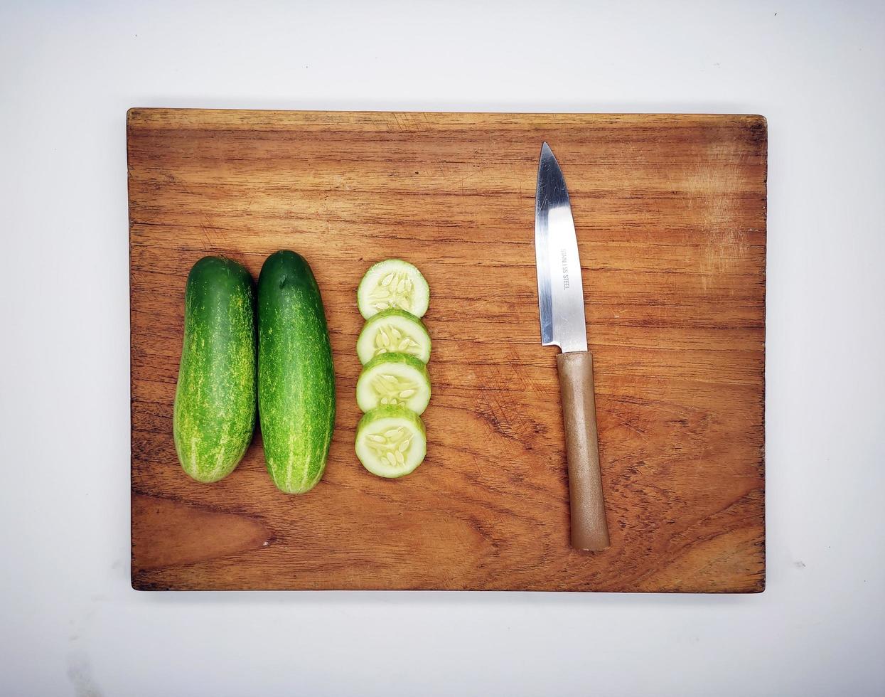 Cucumbers on a wooden cutting board and kitchen knife. photo