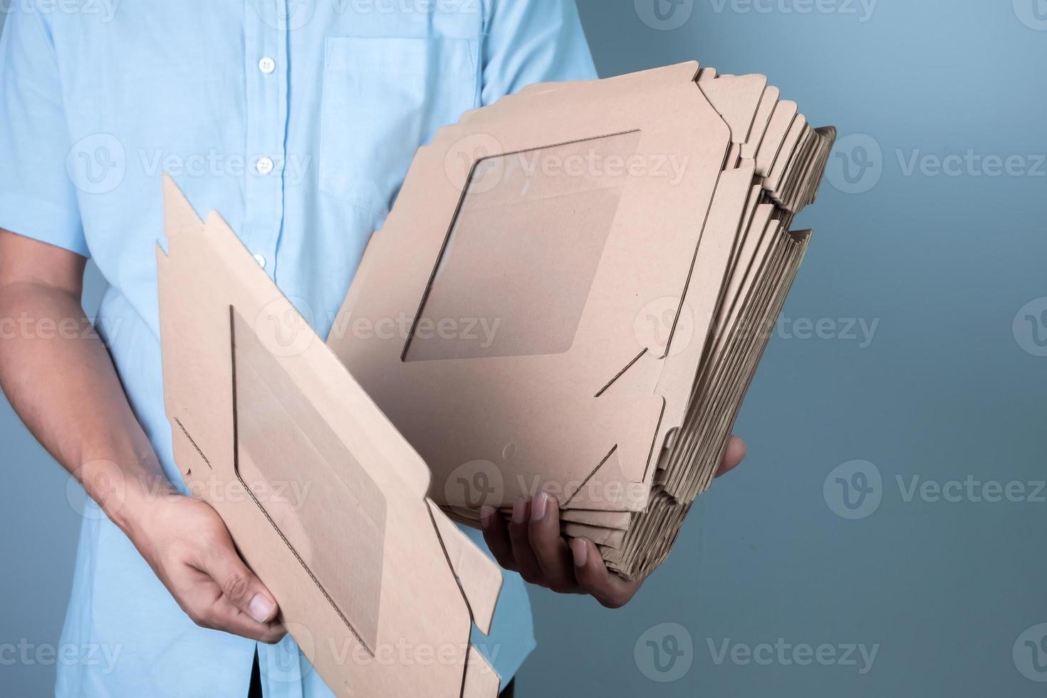 Male hand holding brown cardboard box on blue background, food delivery and packaging concept photo