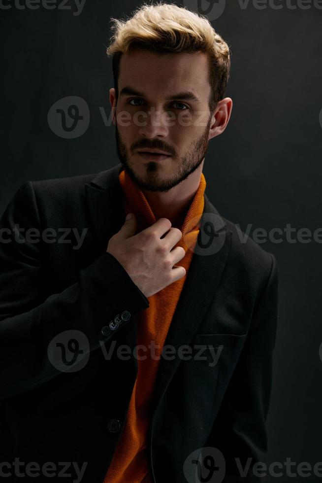 retrato de un atractivo rubio hombre en un oscuro antecedentes en un naranja suéter y Saco foto