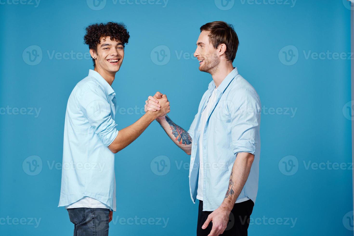 Happy friends in identical shirts shake hands on a blue background communication photo