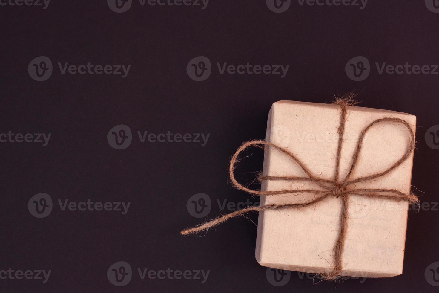 Box with a gift made of kraft paper tied with hemp rope. Dark background with a red tint. Copy space. photo