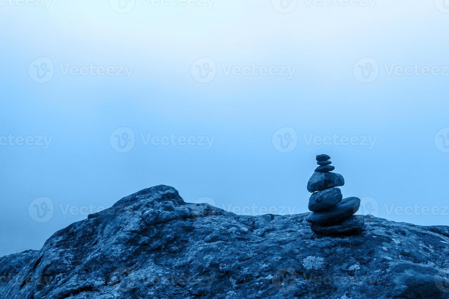 Minimalism. A small cairn stands on a large boulder with dense fog in the background. Blue tinting in color 2020. Horizontal. photo