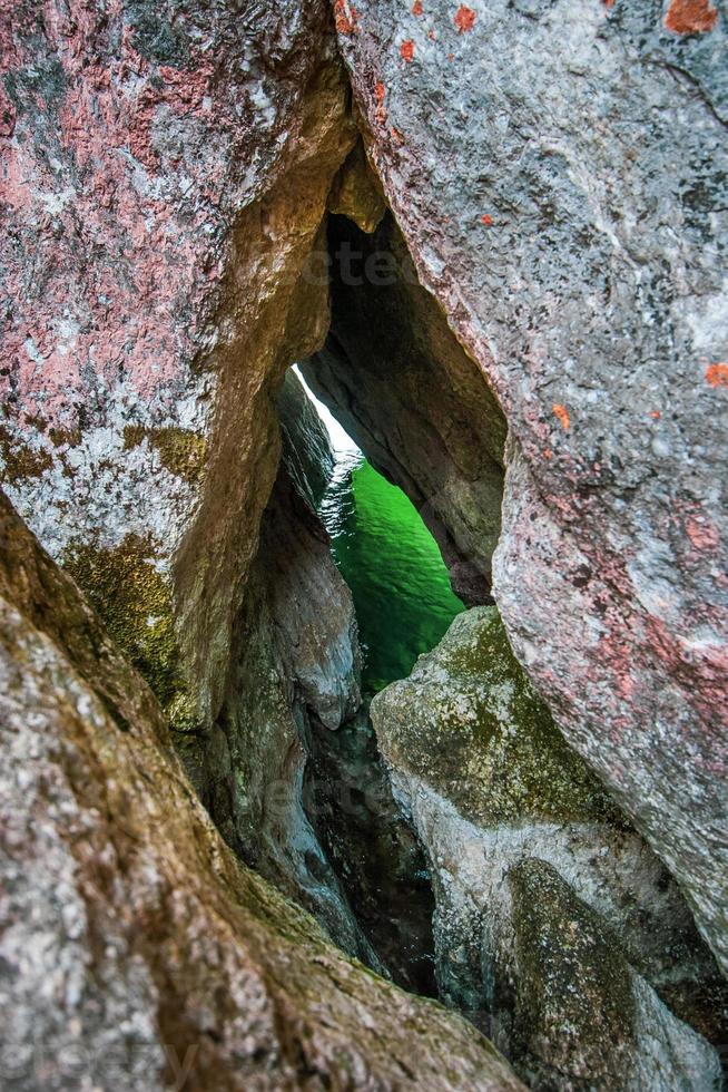 Green water is visible through a narrow gap in a granite rock. Moss on stones. Vertical frame. photo