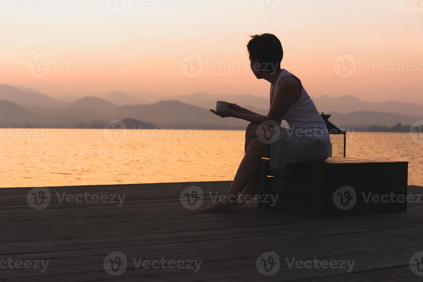 Silhouette woman holding cup coffee sitting by the lake watch sunrise. photo