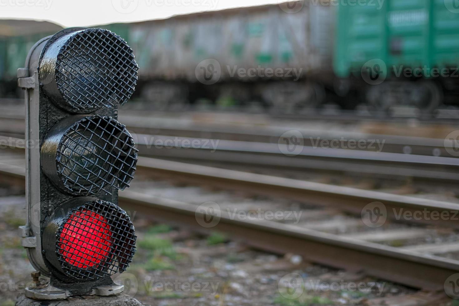 Semaphore with a glowing red lamp close-up. Selective focus on the semaphore. Background with rails and wagons blurred. photo