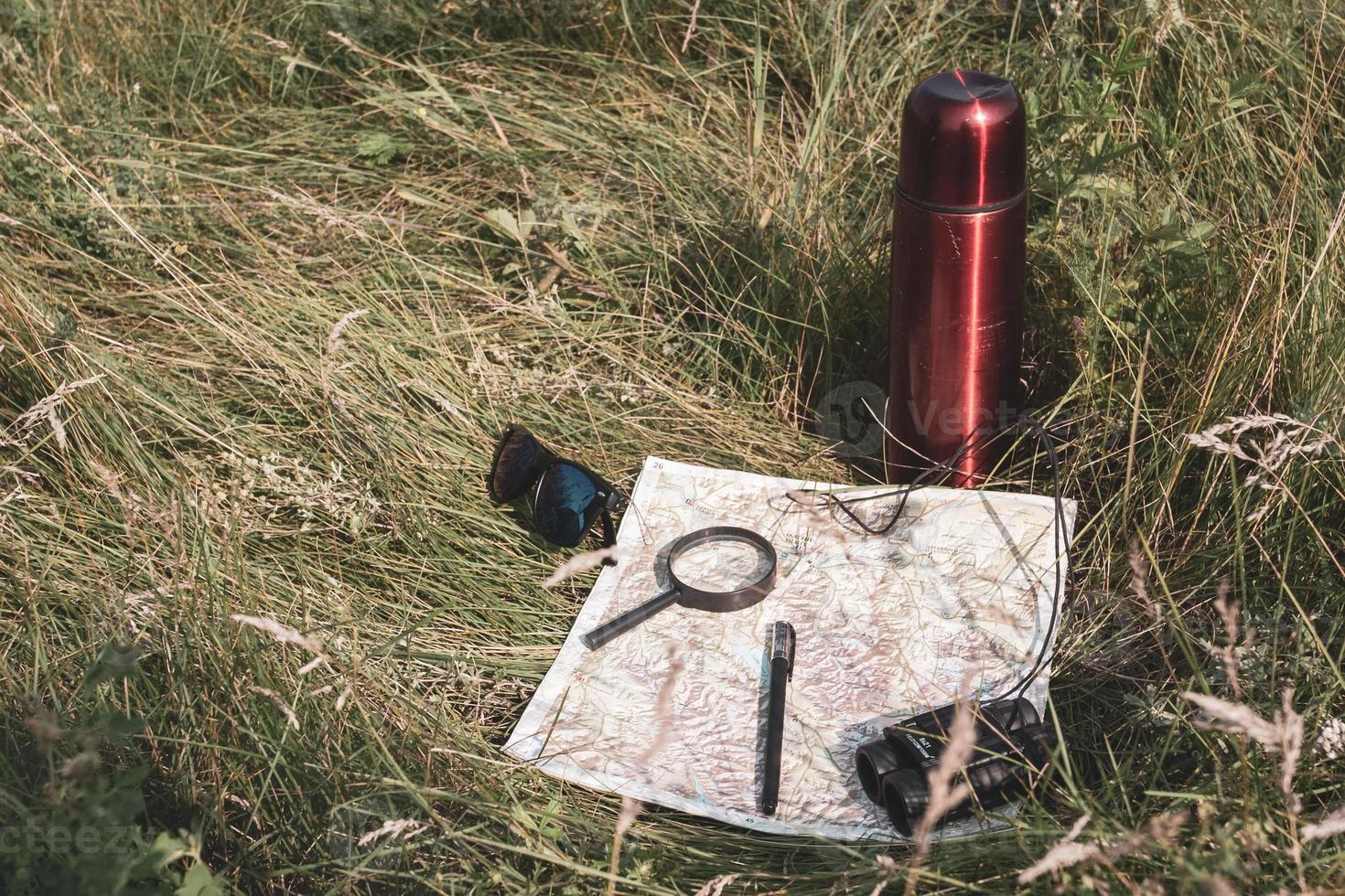 Map, magnifier, binoculars, pen, glasses and a thermos in the grass. Still life of a traveler. photo