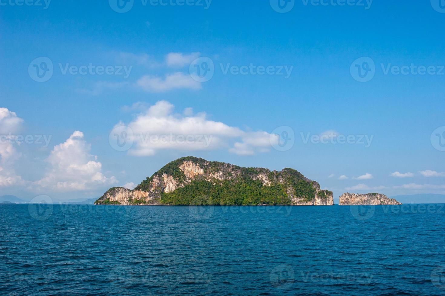 Rocky island in the sea against the blue sky with clouds. A lot of green trees on the slopes. The weather is sunny. Horizontal. photo