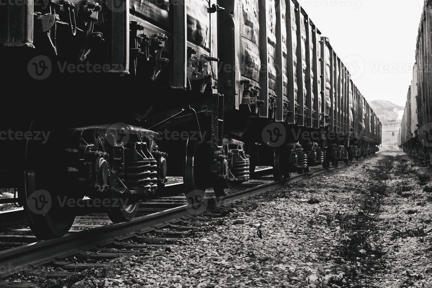 Freight wagons closeup on rails. Stylized black and white photo. A long train, many pairs of wheels with springs. photo