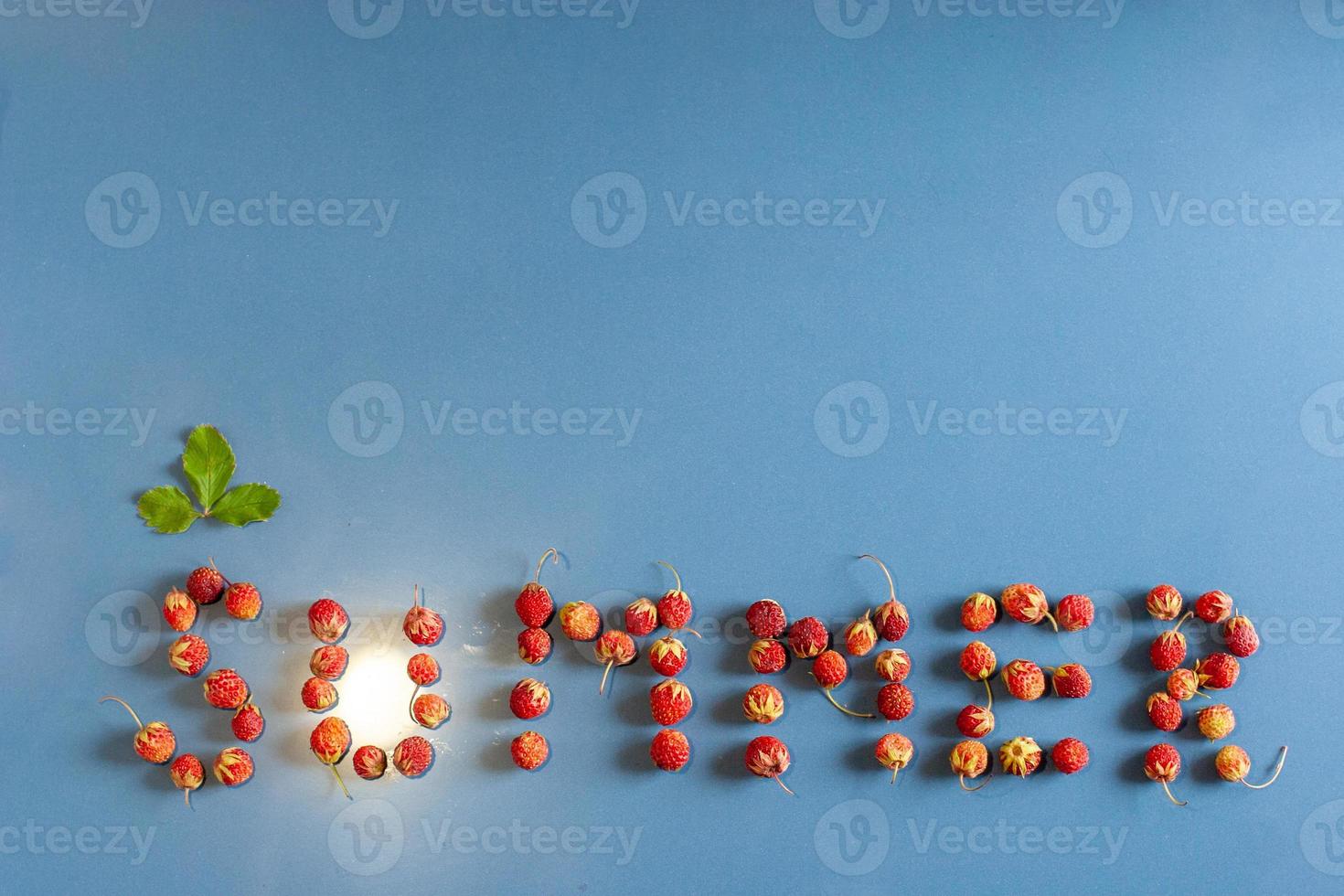 The inscription summer lined with strawberries on a ceramic tile with a dust texture. A leaf above the letter C. Light from a light bulb like the sun in the letter U. Flat view. Forest strawberry. photo