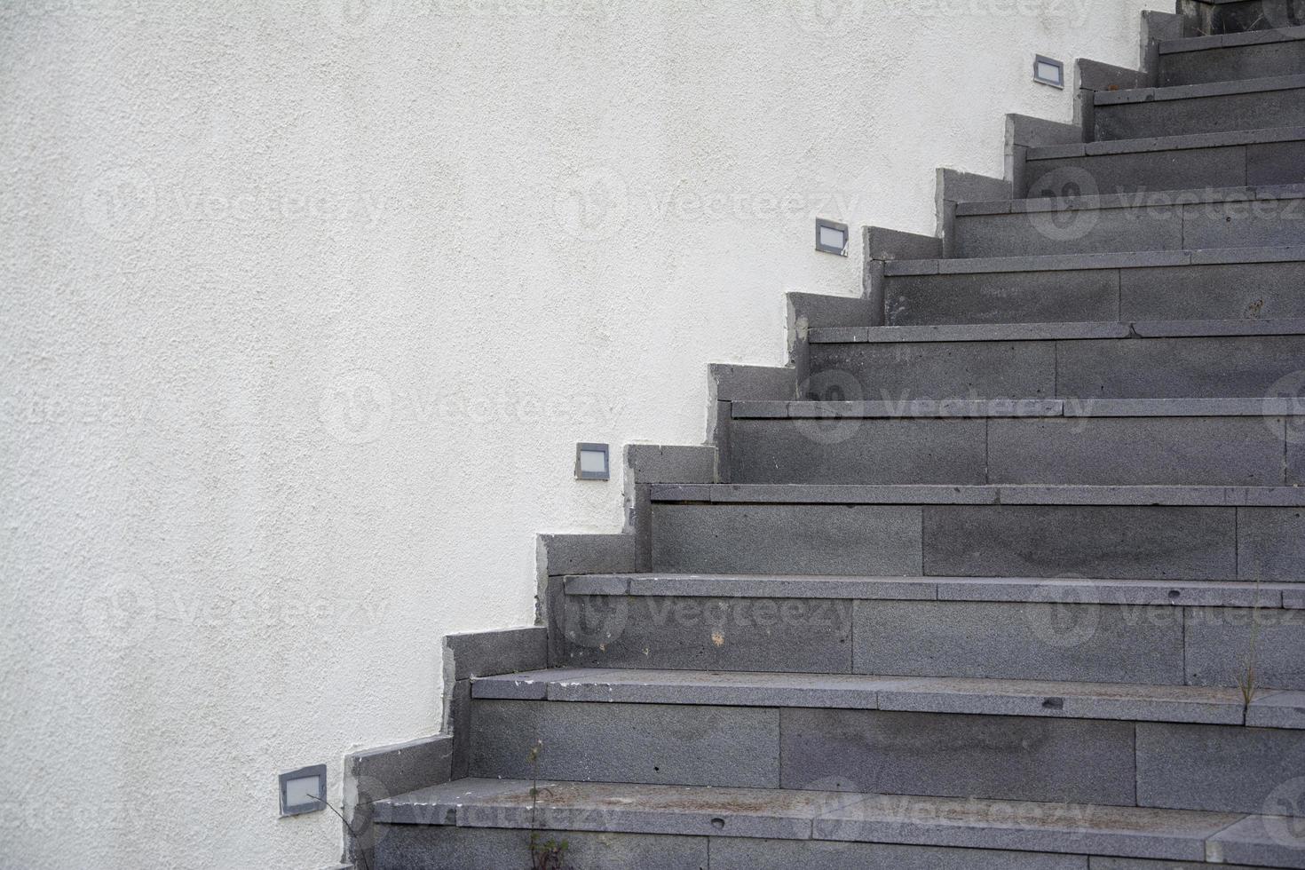 The staircase on the white wall of the building in the park, the gray stone staircase on the white cement wall background. photo