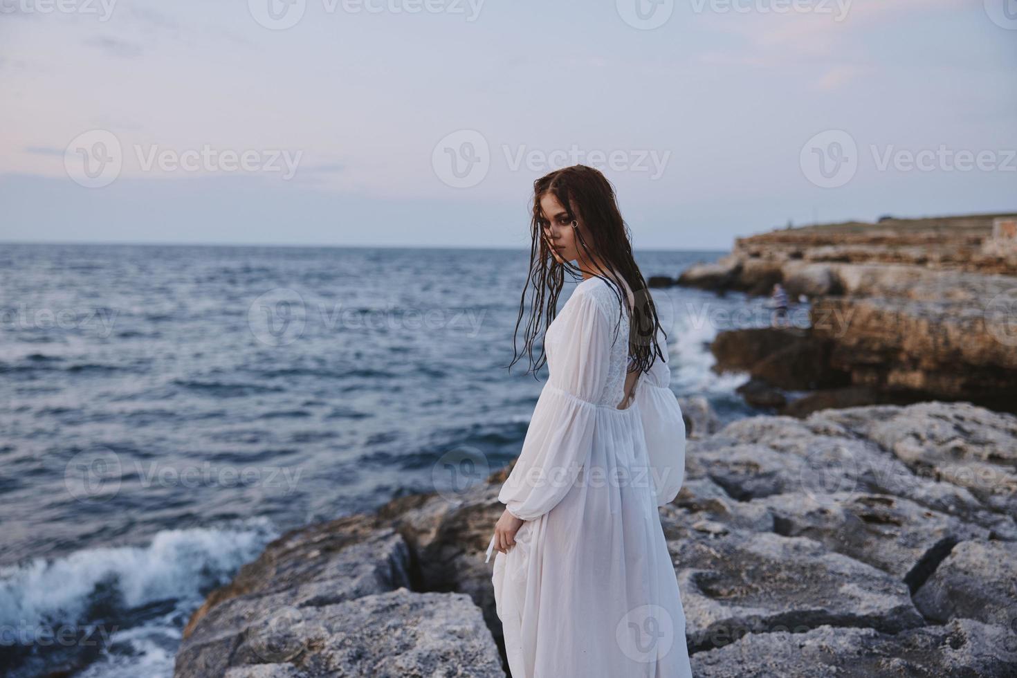 mujer en blanco vestir y paseo a lo largo el océanos Roca playa foto