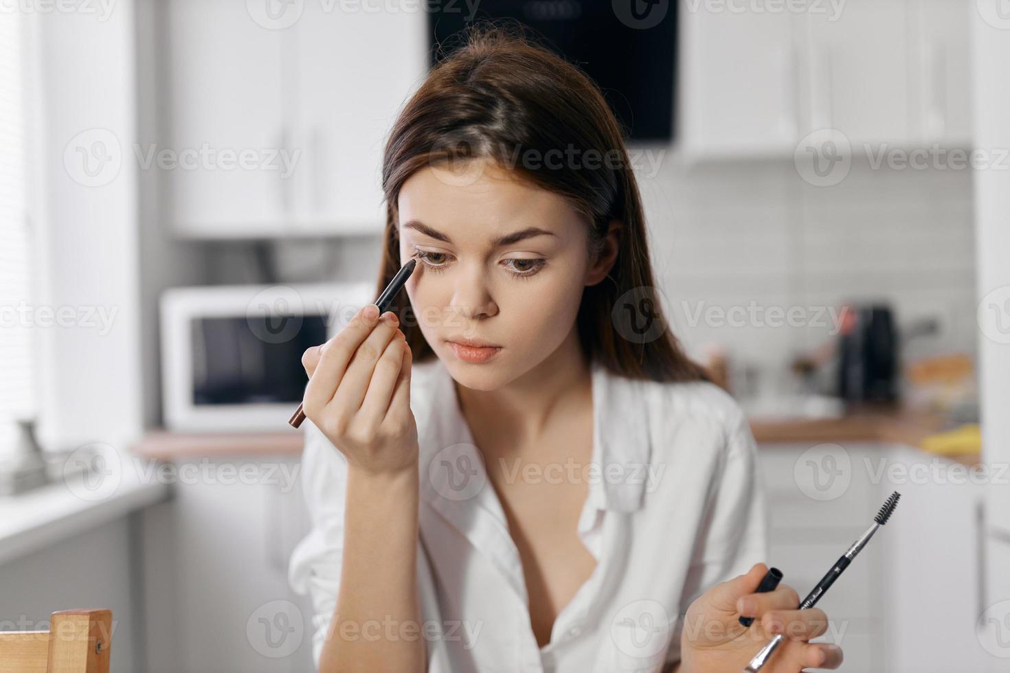 mujer en cocina haciendo maquillaje con delineador de ojos lápiz en mano foto