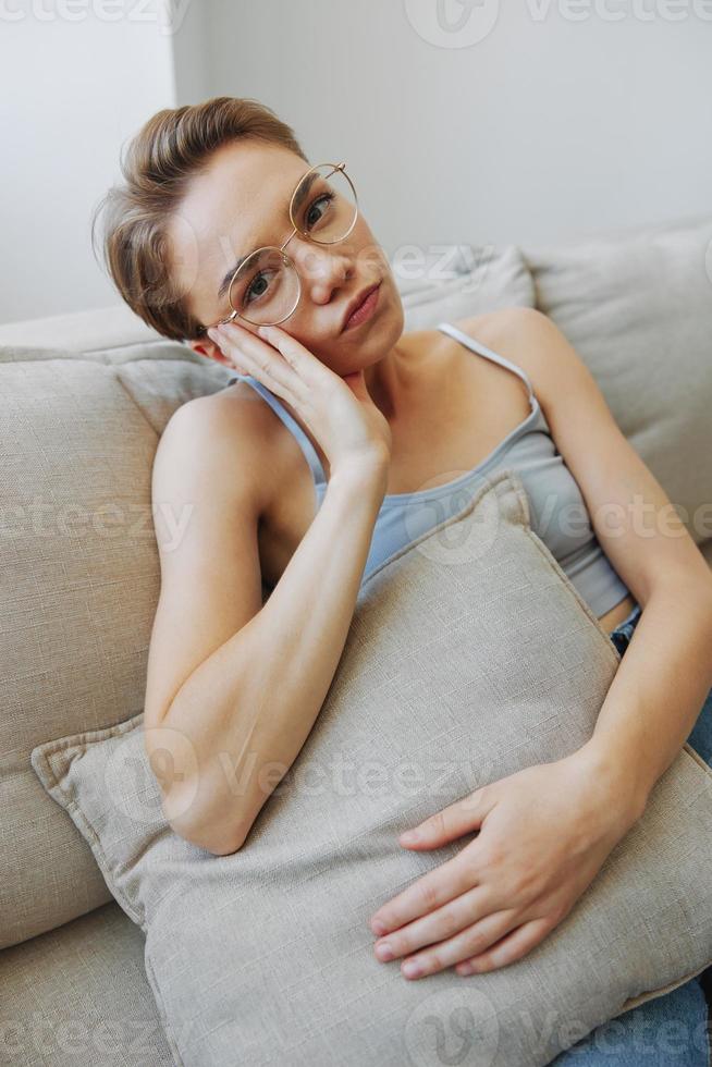 A woman wearing eyeglasses sits on a couch and looks at the camera. Vision problems photo