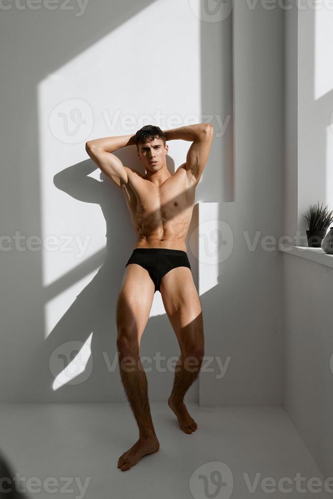 man with pumped up naked body in black panties posing near the window photo
